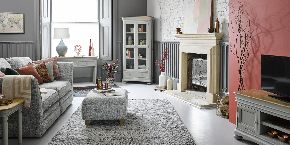 A large cosy living room with grey and red walls and lots of soft grey textured furnishings, a tv, and some beautiful ceramic pots and lamps. 